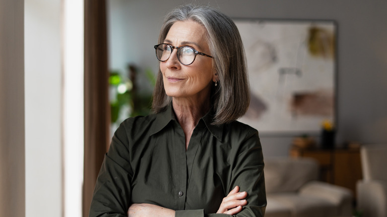 A woman wearing glasses with a gray streak in her lob crossing her arms and looking to the side.