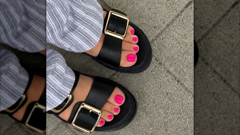 Closeup of a woman's feet, wearing hot pink nail polish and chunky black sandals
