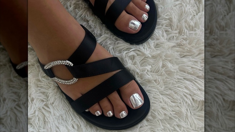 Closeup of a woman's feet with a silver chrome pedicure, wearing black sandals