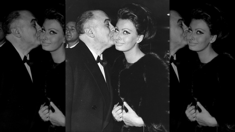 Black-and-white photo of Carlo Ponti kissing his wife, actress Sophia Loren in 1965.