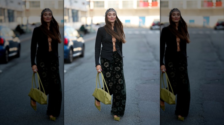A woman wearing floral velvet trousers, green velvet heels, and a black lace-up blouse.