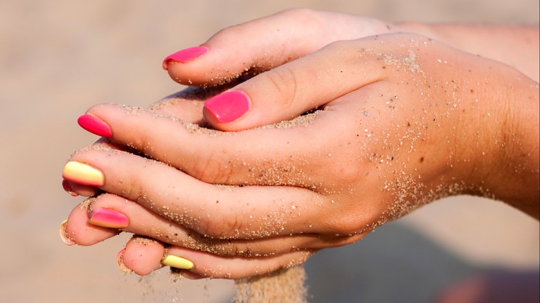 Tan manicured hands holding sand
