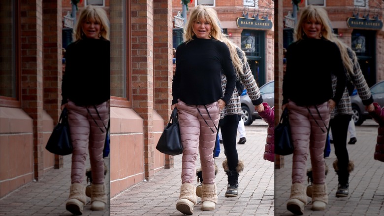 Goldie Hawn walks wearing quilted pink snow pants and a black sweater