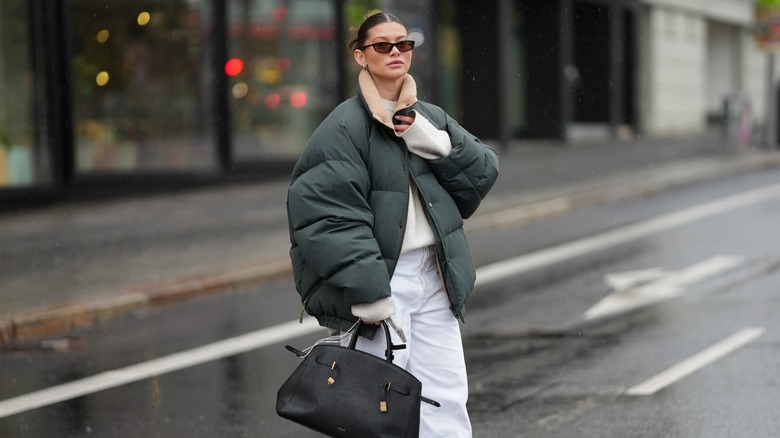 A woman poses in an oversized puffer jacket and narrow brown sunglasses.