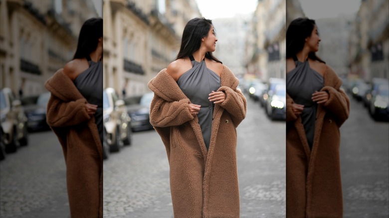 A woman wearing a long teddy bear coat off-the-shoulder.