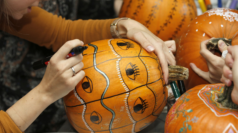 Woman decorating pumpkin with paint marker