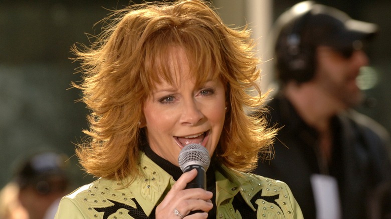 Reba McEntire sings and sports a layered fringe haircut while wearing a light green leather jacket