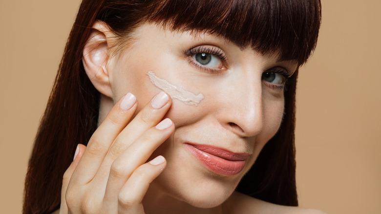 Woman applying tinted moisturizer to face
