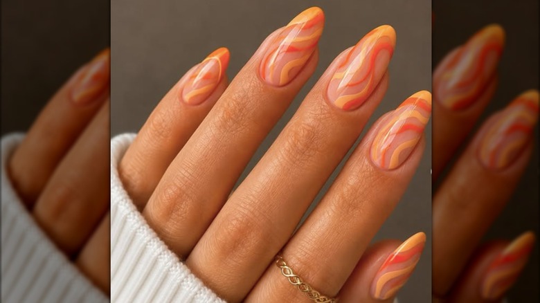 Almond-shaped manicure painted with swirls of light and dark orange polish