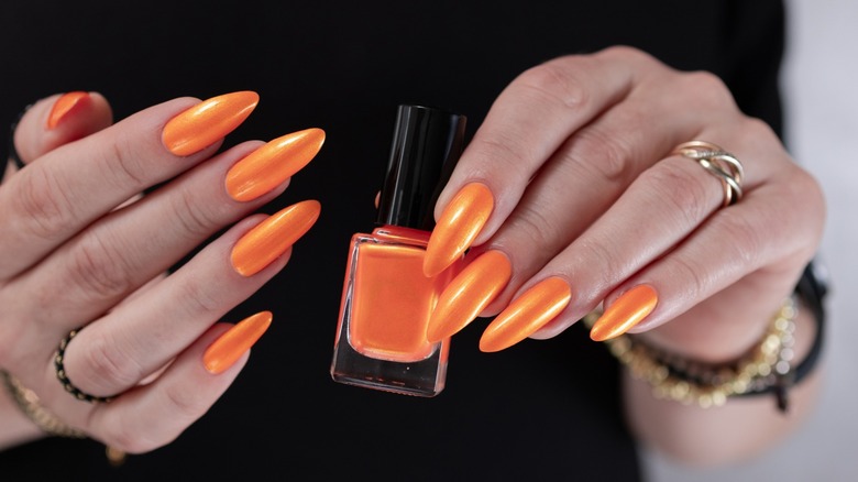 Hands with bright orange manicure holding a bottle of orange nail polish
