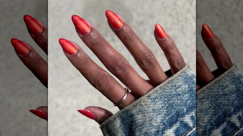 A hand wearing burnt-orange shimmer nail polish.
