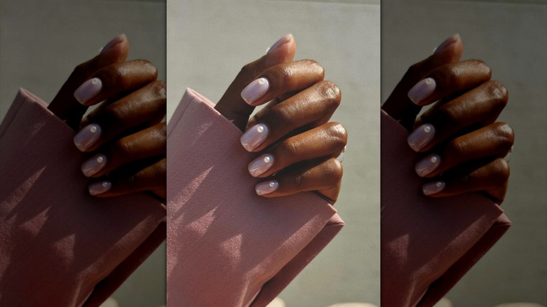 A hand wearing nude-pink nail polish with pearl accents.
