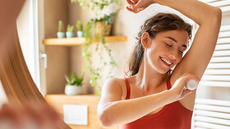 Woman applies deodorant in mirror 