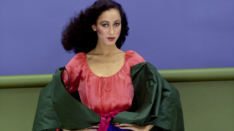 Pat Cleveland wearing Oscar de la Renta's jewel-toned blue silk taffeta skirt and green jacket with an orange satin peasant blouse