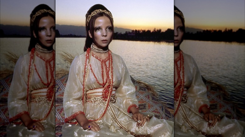 Model Penelope Tree sits on the bank of a Kashmir lake at dusk wearing a shimmering caftan detailed with coral beads and cinched with a gold belt