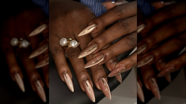 Long pointed manicure with gold cat eye nail polish and gold stripe designs