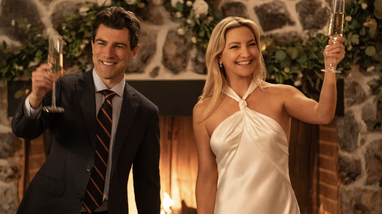 Kate Hudson in a an ivory Galvan halter neck dress standing next to Max Greenfield holding up champagne glasses.