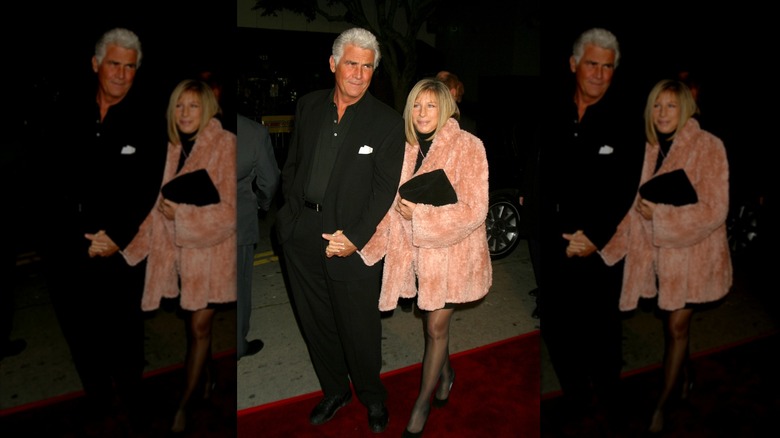 Barbra Streisand wearing a fuzzy pink coat holding hands with husband James Brolin wearing an all-black suit.