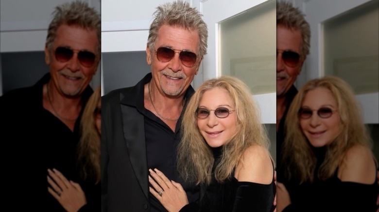 A candid photo of Barbra Streisand wearing a black top and sunglasses posing next to husband James Brolin also wearing black and sunglasses.