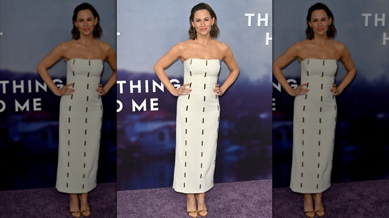 Jennifer Garner with her hands on her hips wearing a white strapless dress with dash designs at a red carpet event.