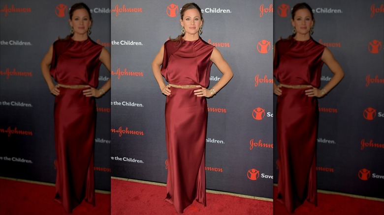 Jennifer Garner posing on a red carpet wearing a ruby-red satin gown with a tan belt.