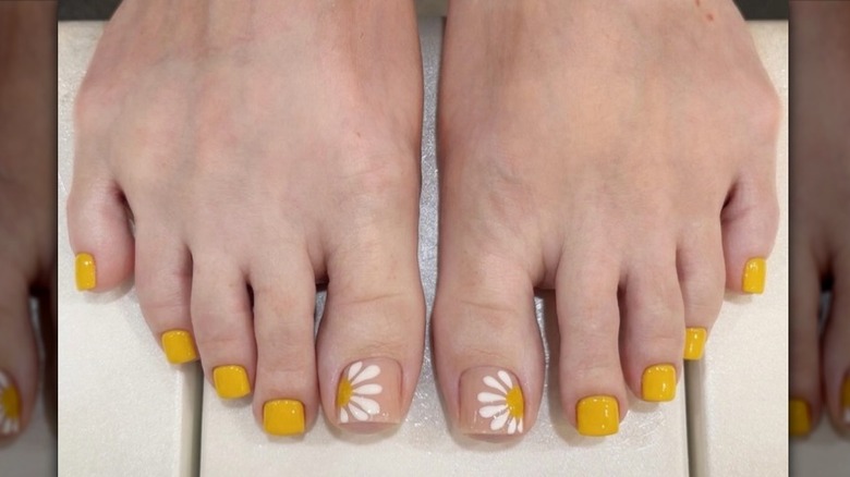 Close up to a mustard yellow pedicure with daisy accent toe