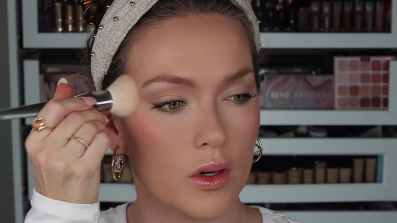 Woman looking off camera and applying blush while wearing a headband.