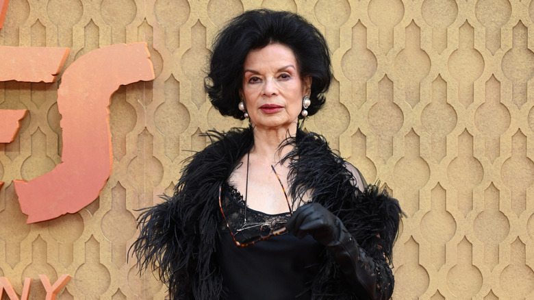 Bianca Jagger wears a black dress and feathered jacket.