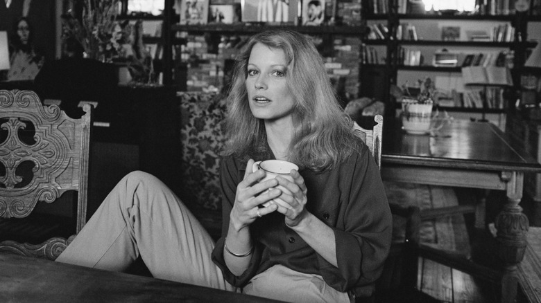 A black-and-white portrait of Shelley Hack holding a mug.