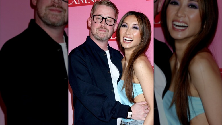 Macaulay Culkin in a navy blue button down standing next to Brenda Song in a turquoise tube top.