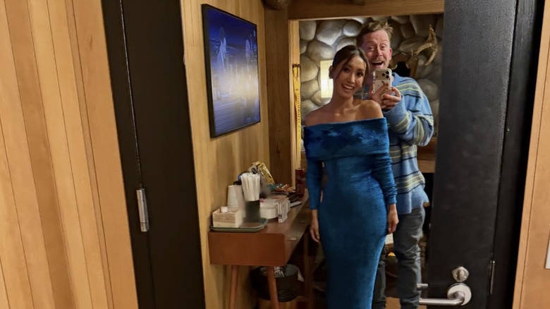 Brenda Song wearing a blue suede gown while Macaulay Culkin is standing behind her in a cozy sweater and jeans.