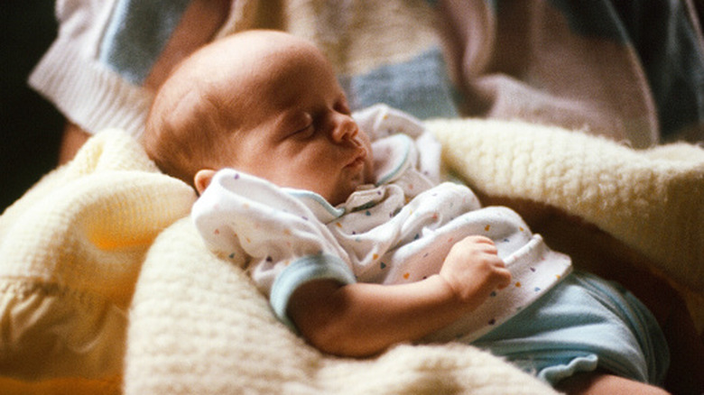 A newborn baby sleeps on a yellow blanket