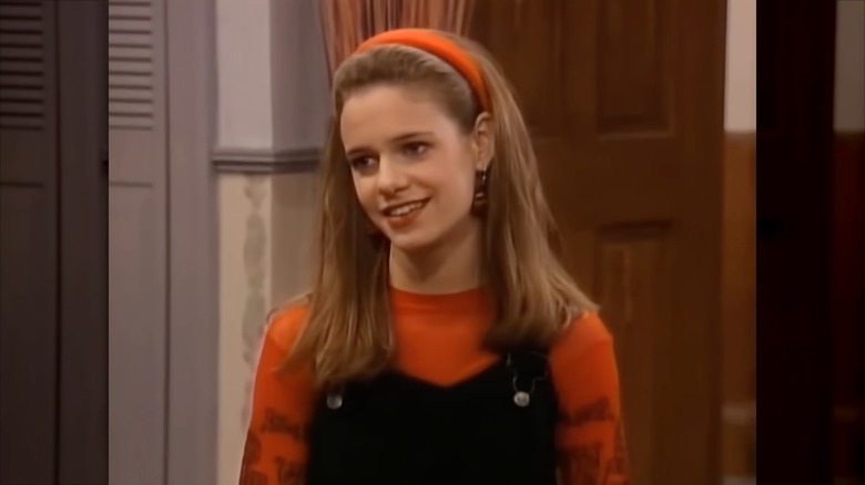 Andrea Barber wearing an orange headband, an orange top, and black dungarees
