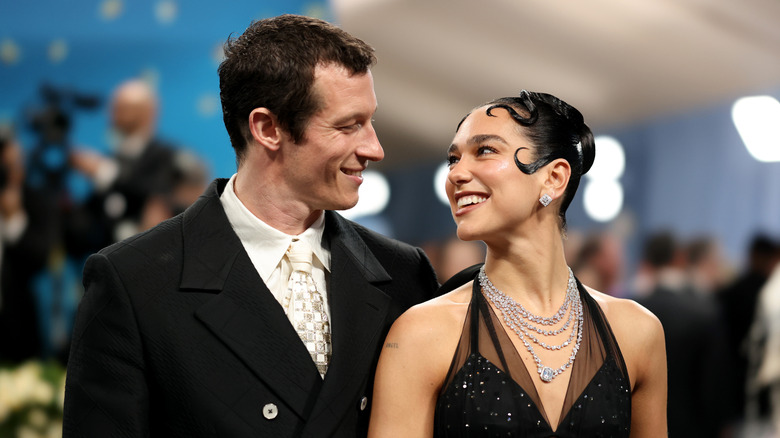Callum Turner and Dua Lipa smile at each other on a red carpet