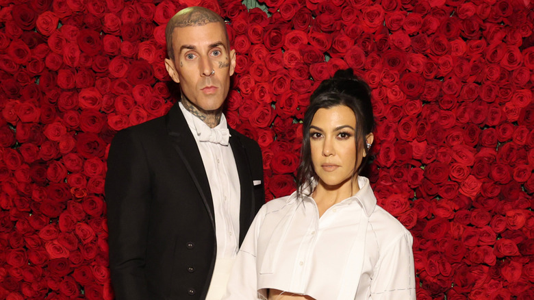 Travis Barker and Kourtney Kardashian pose in front of a red rose wall