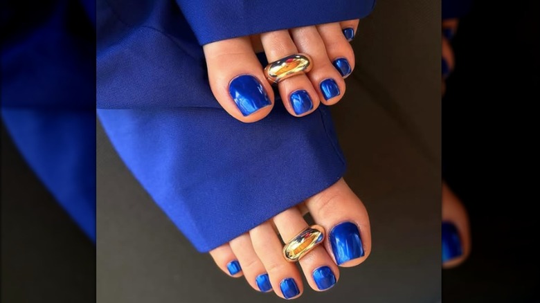 A pedicure with blue chrome nail polish and gold toe rings