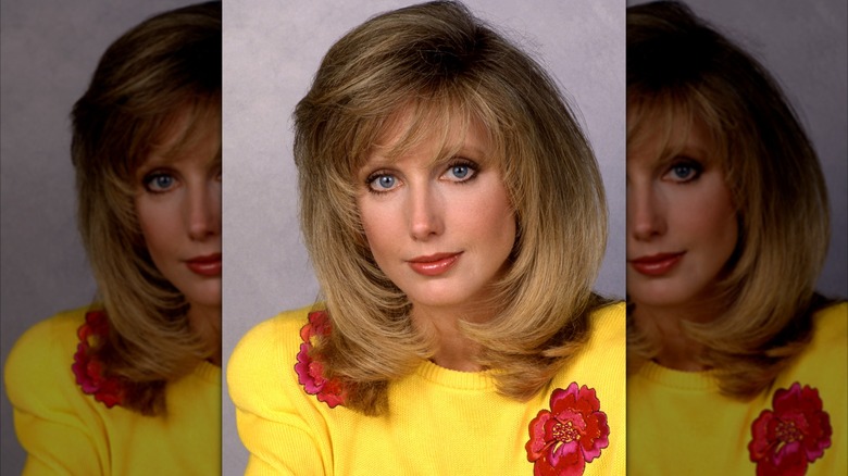 Morgan Fairchild in a 1990 portrait wearing a yellow sweater with red floral accents.