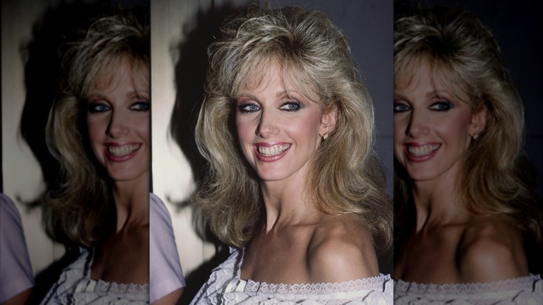 Morgan Fairchild in 1984 smiling in an off-the-shoulder dress with fluffy bangs.