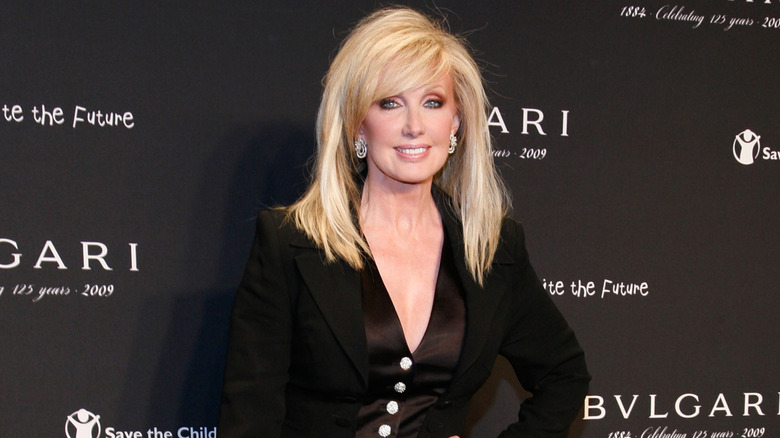 Morgan Fairchild posing at an event wearing a black outfit and diamond earrings.