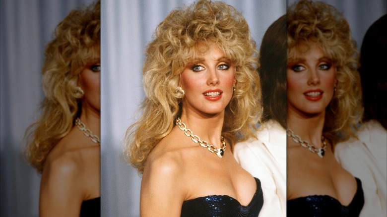 Morgan Fairchild in 1982 at a formal event wearing a sparkly gown and chain necklace with voluminous curly hair.