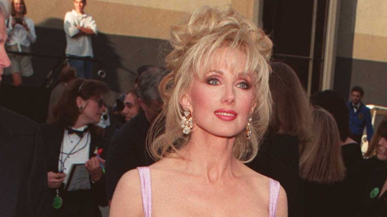 Morgan Fairchild in 1996 on the red carpet with a messy updo and wispy bangs.