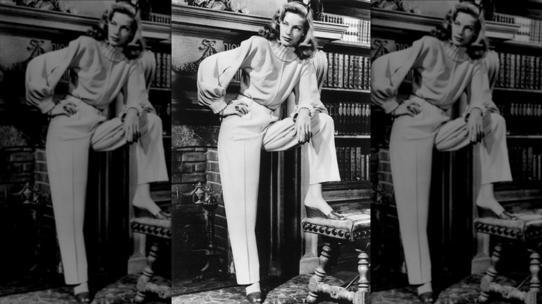 Lauren Bacall poses near a fireplace in a Leah Rhodes turtleneck sweater, relaxed slacks, and wedge mules in December 1946
