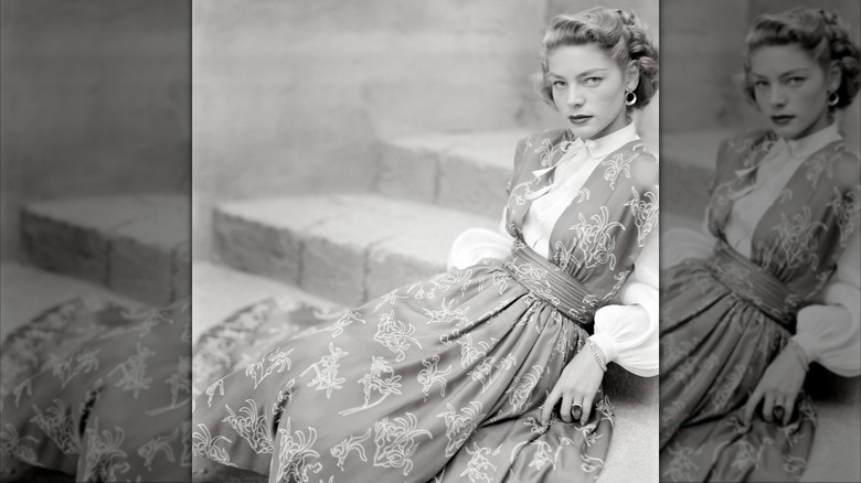 Lauren Bacall lounging on stairs in a white blouse and floral-printed pinafore dress for Glamour magazine in August 1949