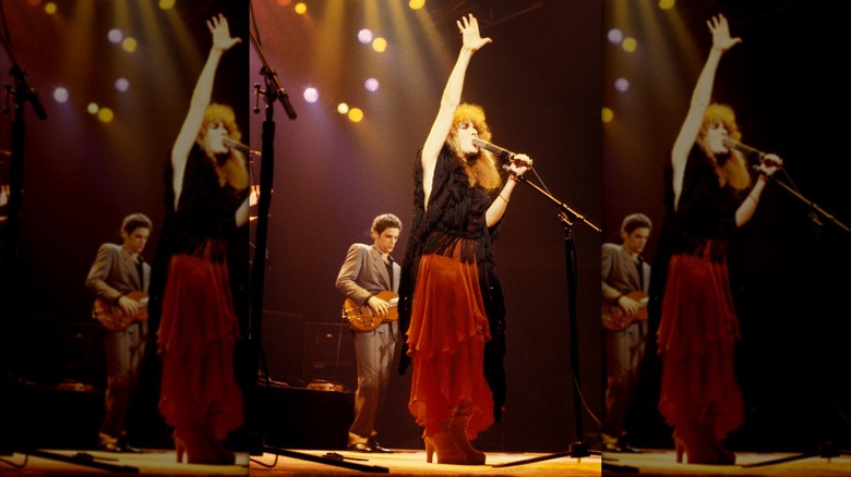 Stevie Nicks on stage with her hand in the air wearing a red skirt and black top performing with Fleetwood Mac in 1979.