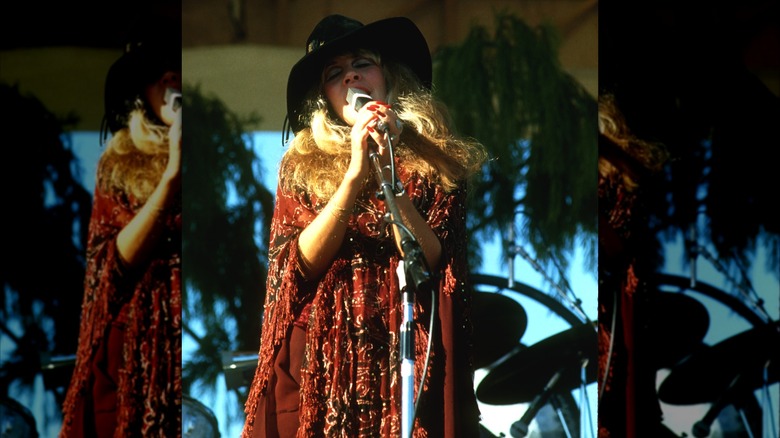Stevie Nicks wearing a black hat and a red outfit performing with Fleetwood Mac in 1977.