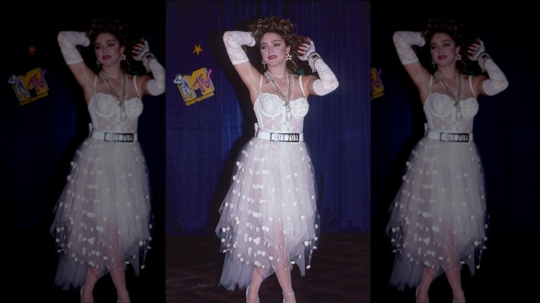 Madonna pictured in 1984 wearing a white lace bodysuit, sheer skirt, and white gloves