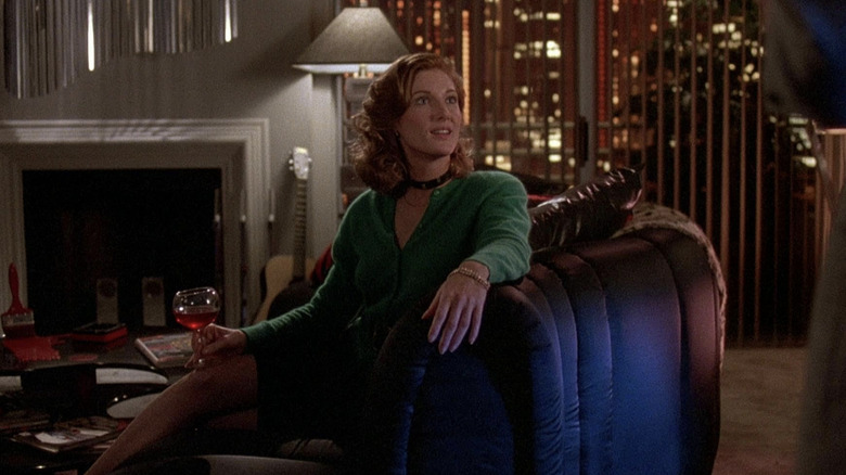 Annette O'Toole sitting on a couch holding a glass of wine wearing a green shirt with a black choker in "Cross My Heart."
