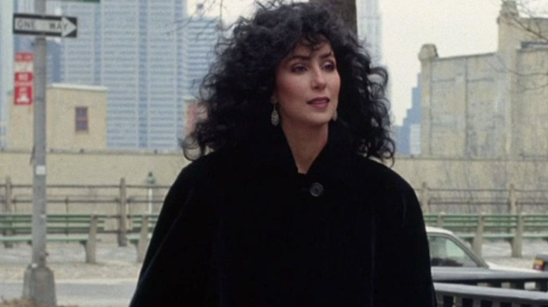Cher wearing a long black coat with curly black hair in 
