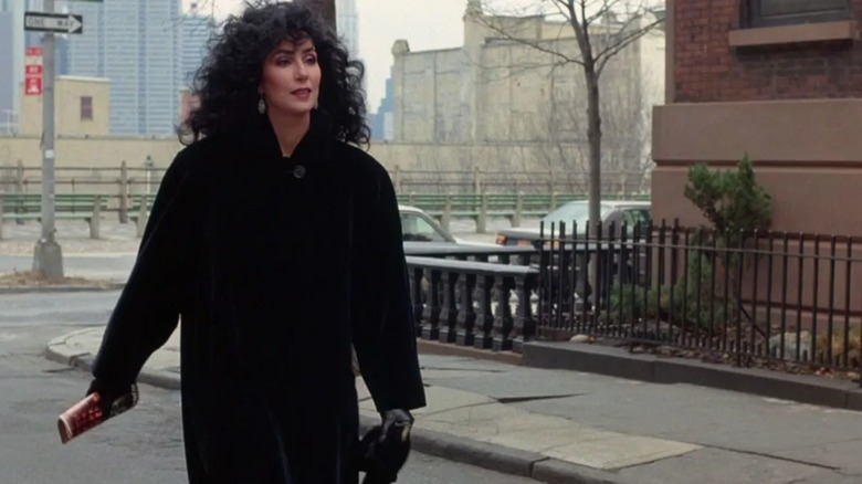 Cher wearing a long black coat with curly black hair on a NYC street in "Moonstruck."