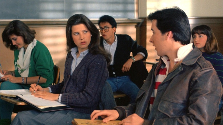 Daphne Zuniga sitting at a school desk wearing a blue button-up shirt with a blue knit sweater in "The Sure Thing."